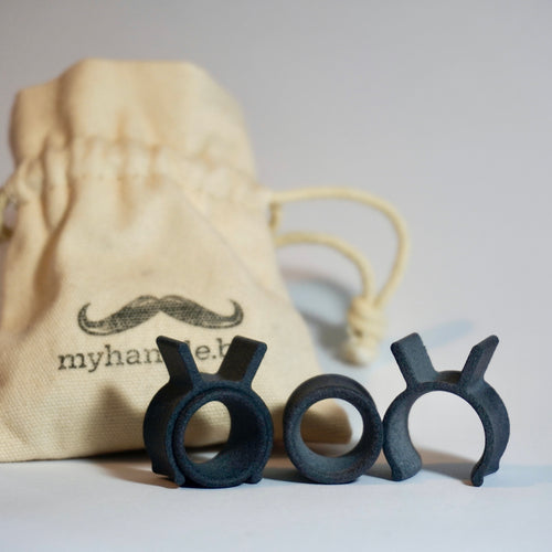 Black myhandle.bar Training Wheel v2 handlebar moustache curling product in front of a beige drawstring bag with 'myhandle.bar' branding.