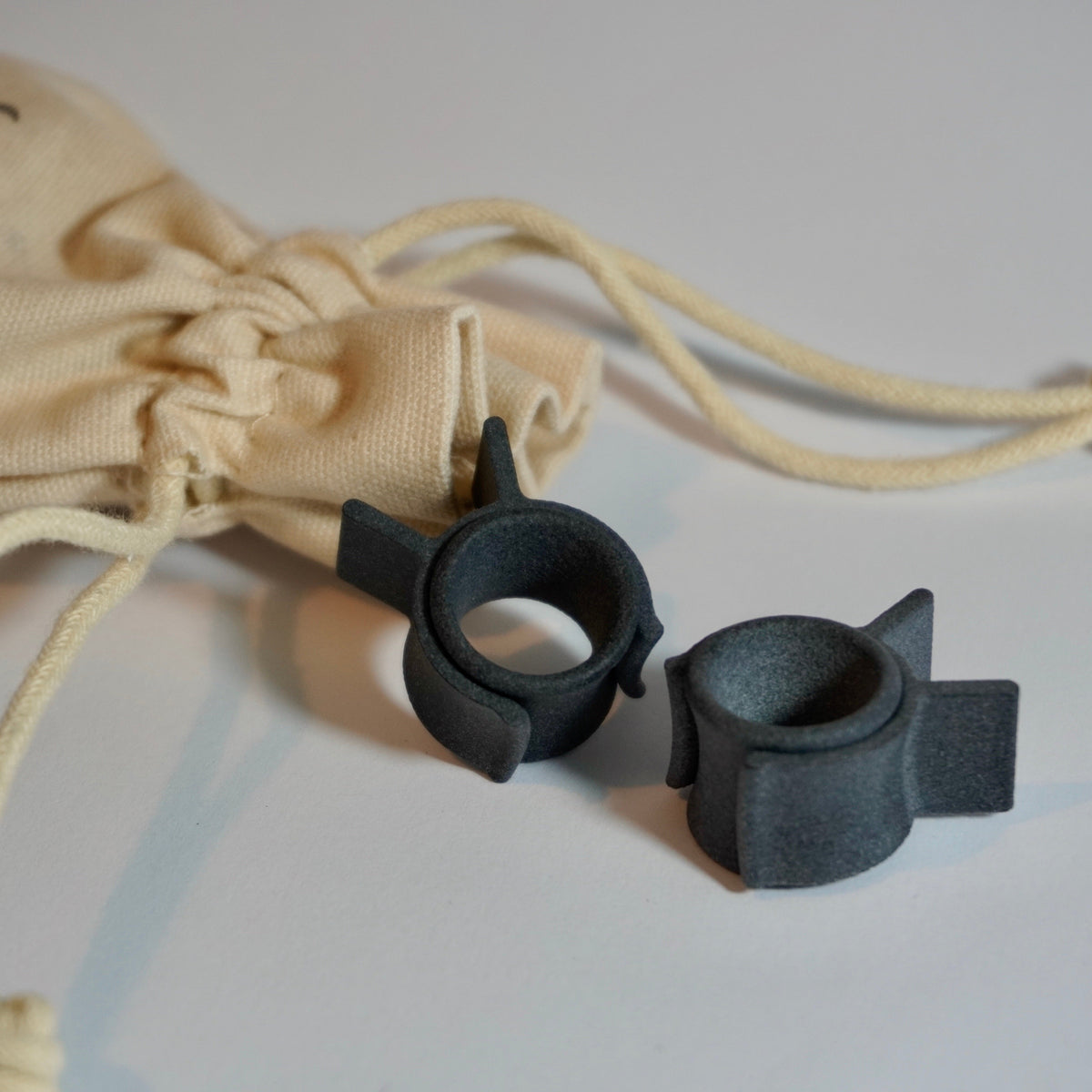 Black myhandle.bar Training Wheels v2 3D printed curlers for styling a handlebar moustache infront of a beige linen travel drawstring bag.