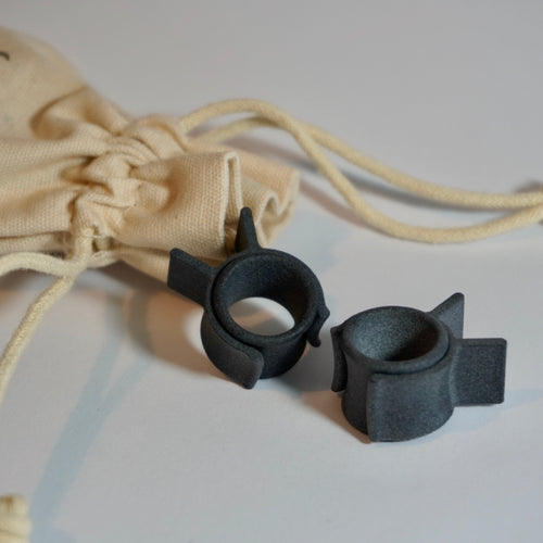 Black myhandle.bar Training Wheels v2 3D printed curlers for styling a handlebar moustache infront of a beige linen travel drawstring bag.